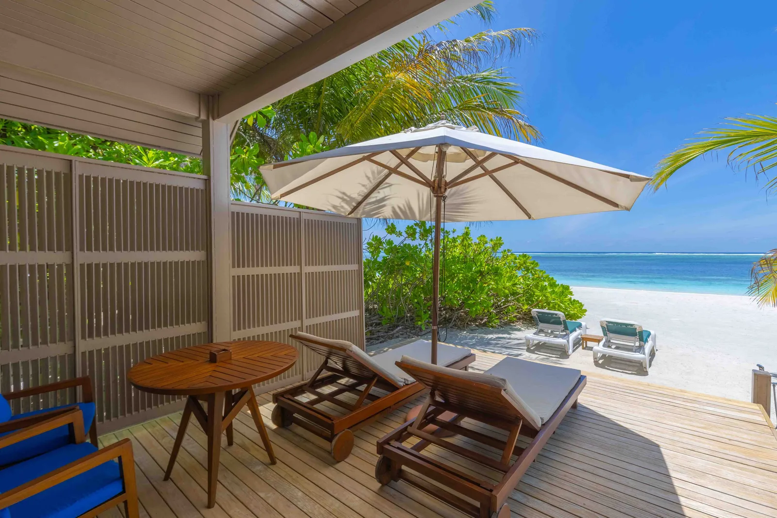 The porch of a Water Front Villa, with a table and loungers on the sand