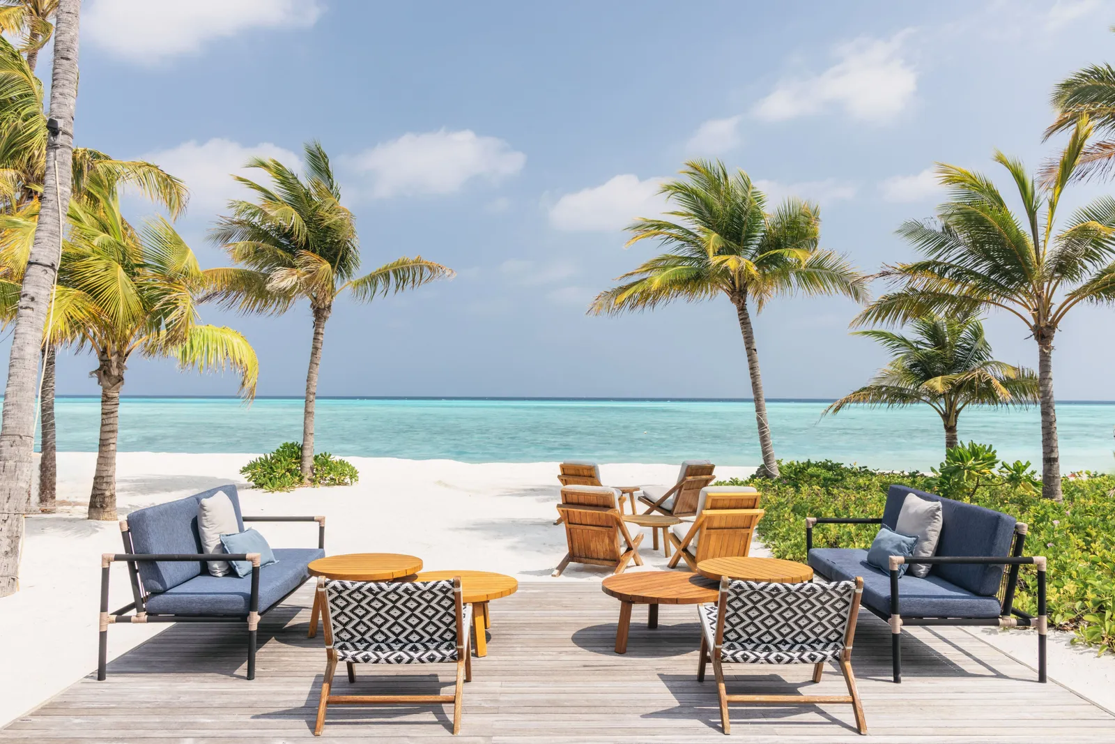 Magical on the beach: blue sofas, armchairs and low tables on the decking, the palms and the turquoise sea.