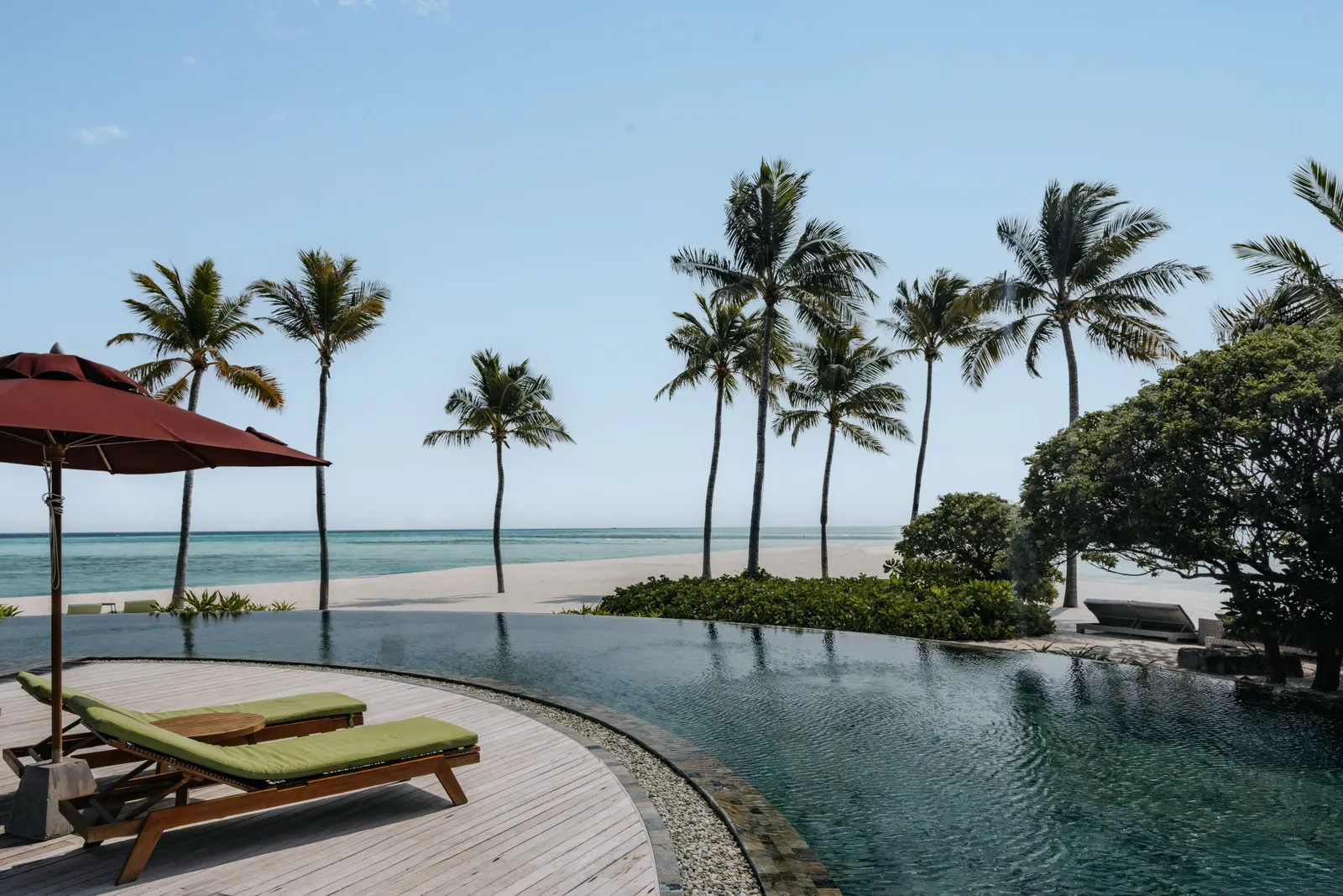 The infinity pool with its curved edge, loungers and a red parasol, the palms and the beach behind.