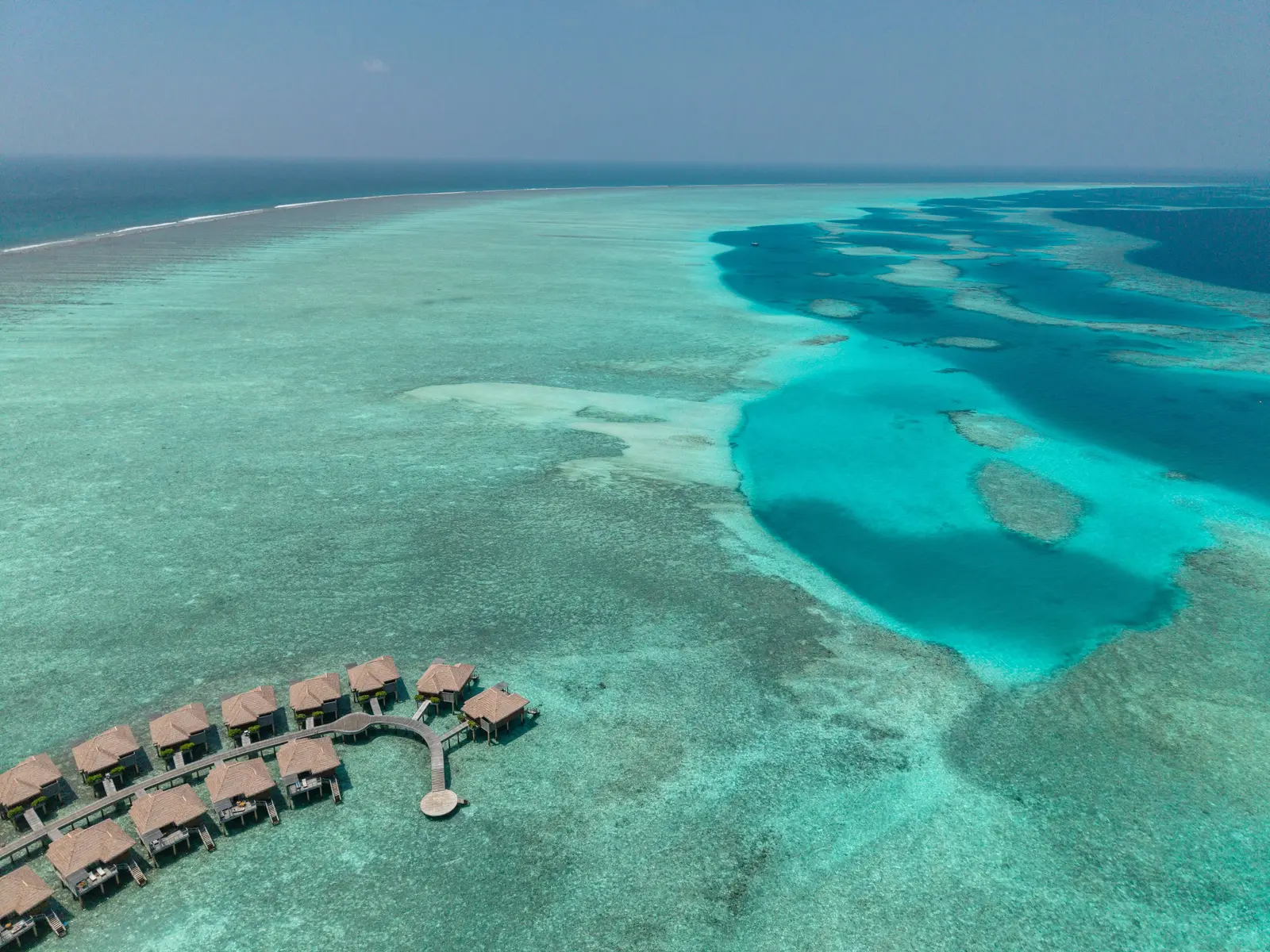 The lagoon from above, the dark patches of reef in the turquoise water and the water villas at the bottom left.