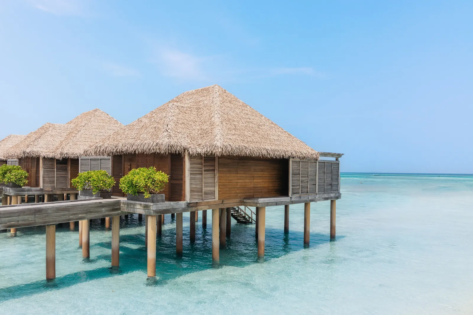 The Sunrise Water Villas on stilts above the turquoise water, with thatched roofs and steps down to the lagoon.