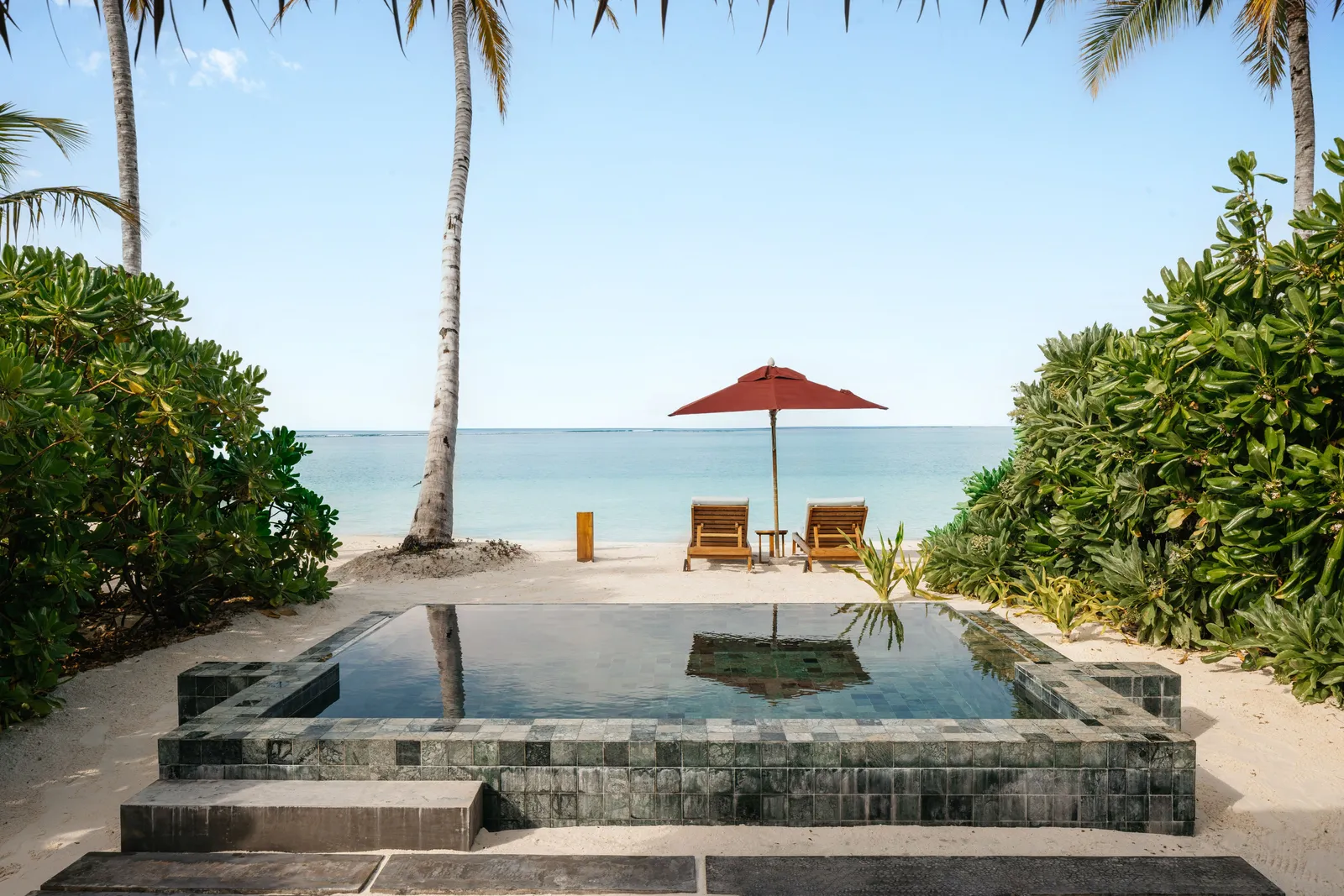 The private pool of a Sunset Suite Villa with Pool, with loungers on the sand and the sea between the palms.