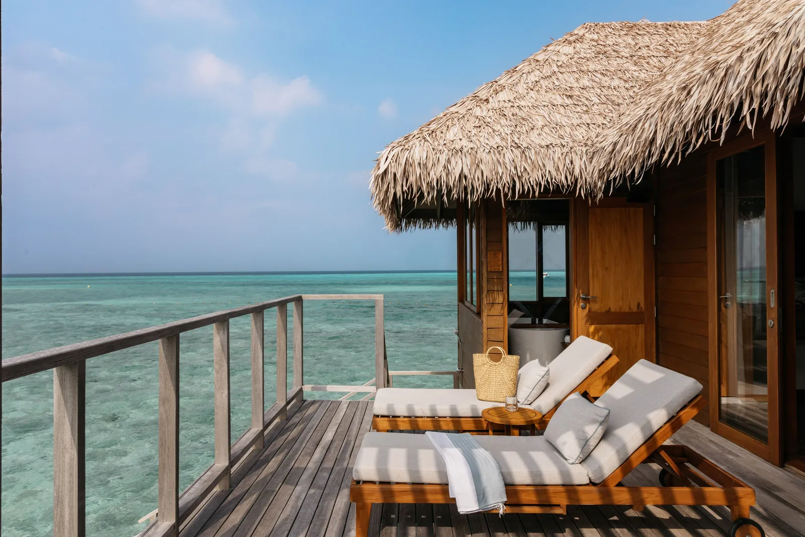 A Sunset Water Villa’s deck, with striped loungers on the timber and the lagoon beyond the railing.