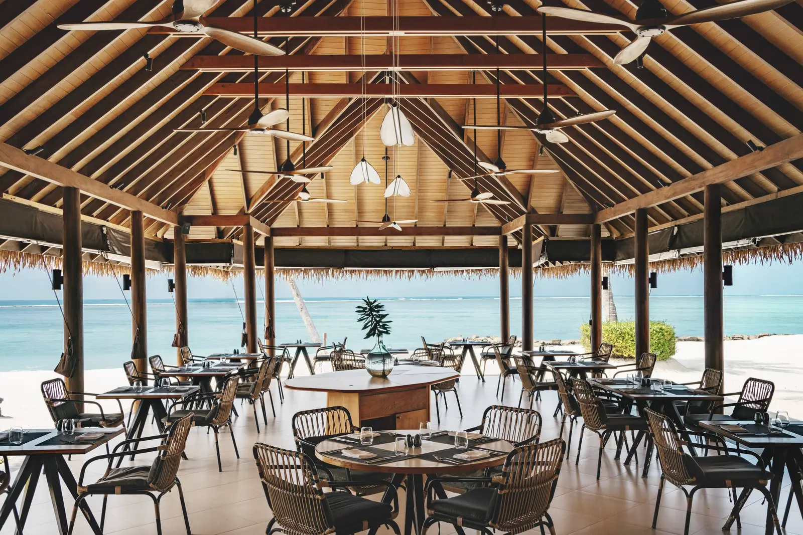 Sea Salt’s dining room under its high timber roof, with laid tables, ceiling fans and the beach beyond the pillars.