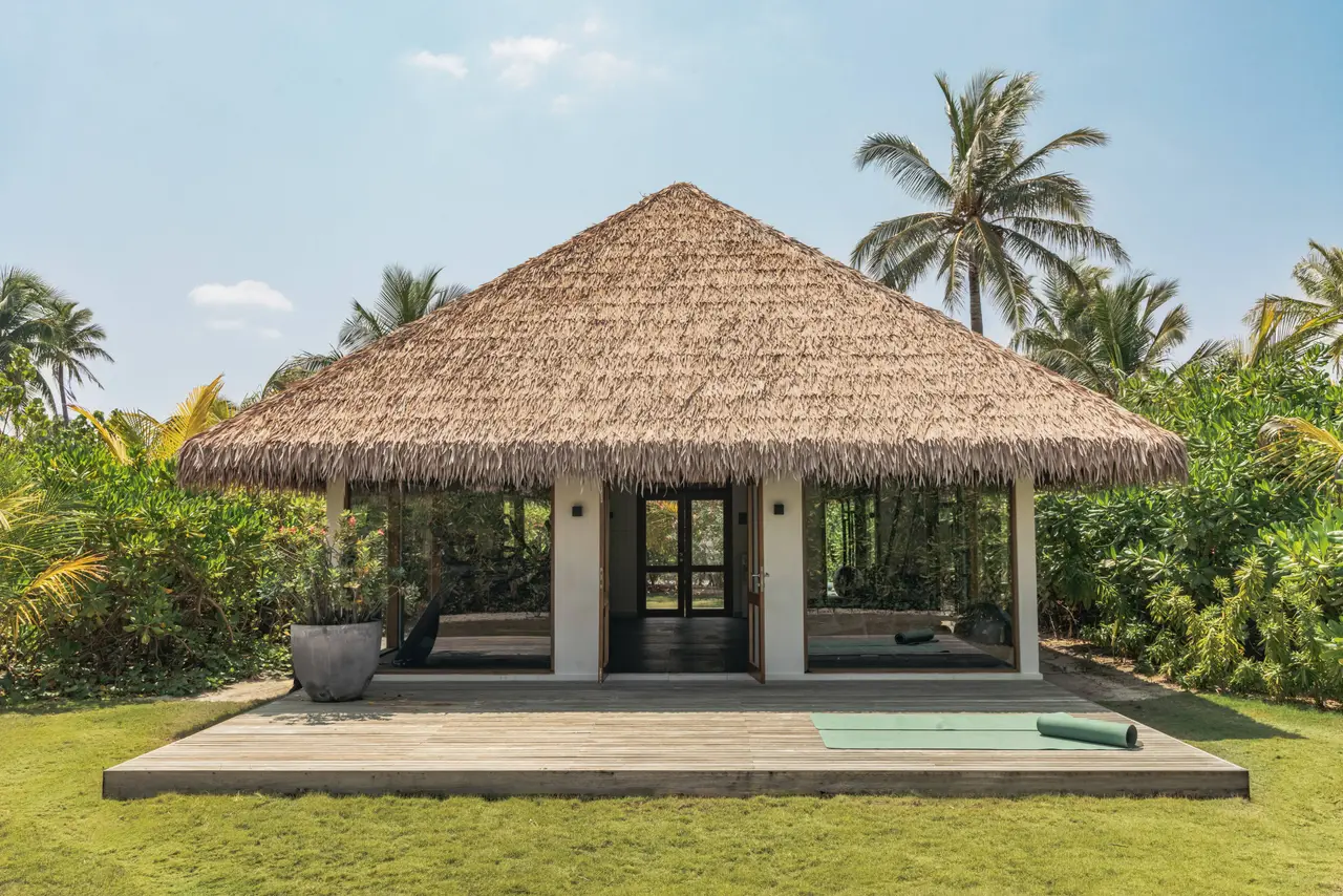 The thatched yoga pavilion with glass walls, on its timber deck between the lawn and the palms.
