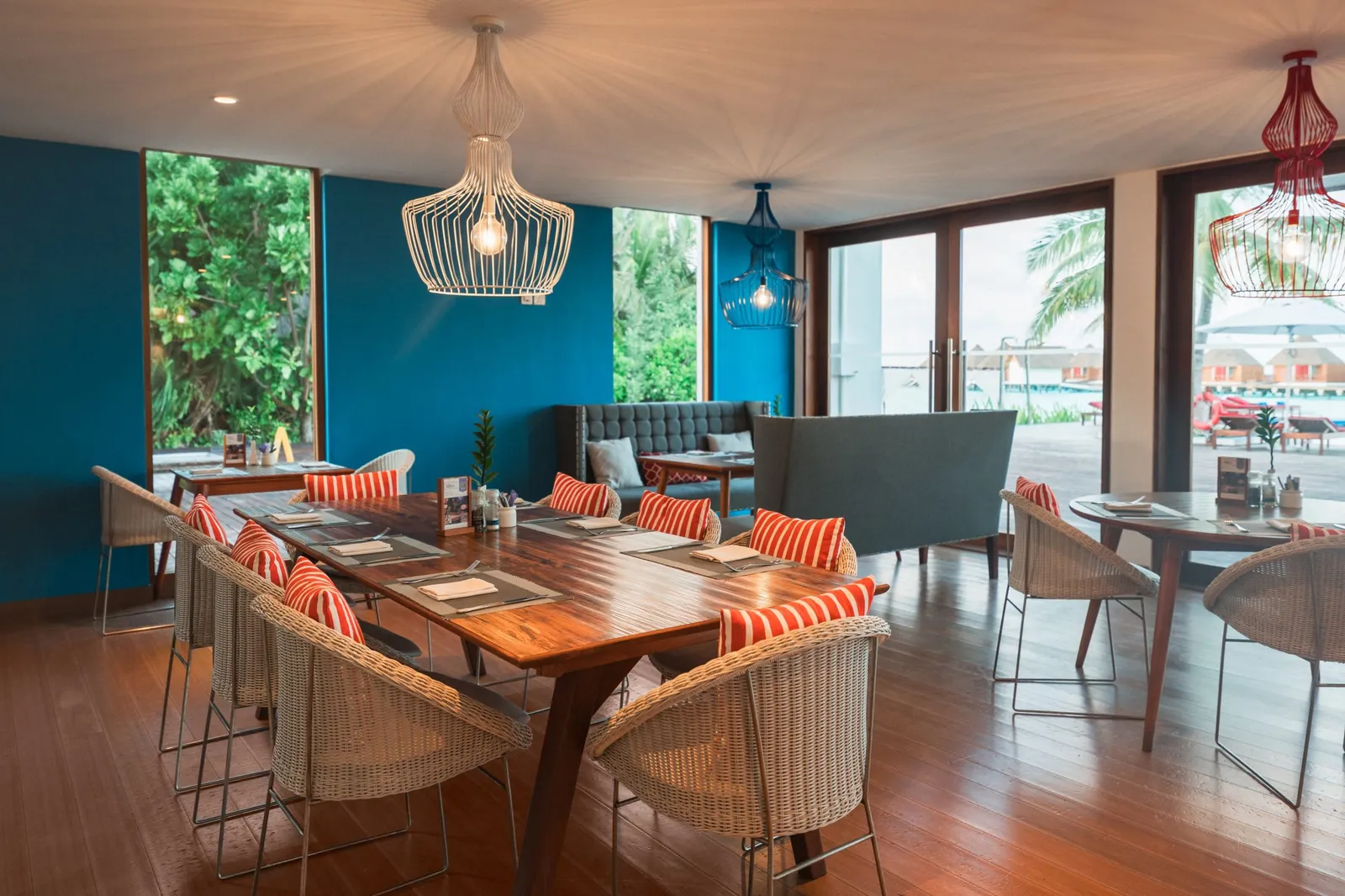 Alita’s dining room, with wooden tables, striped cushions and doors open onto the pool terrace.