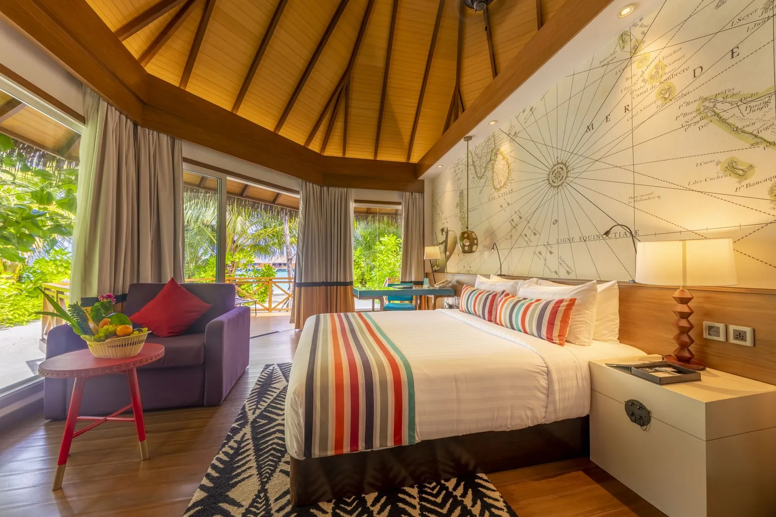 A Beach Villa bedroom: the bed with its striped runner, a sea chart on the wall and glass doors onto the garden.