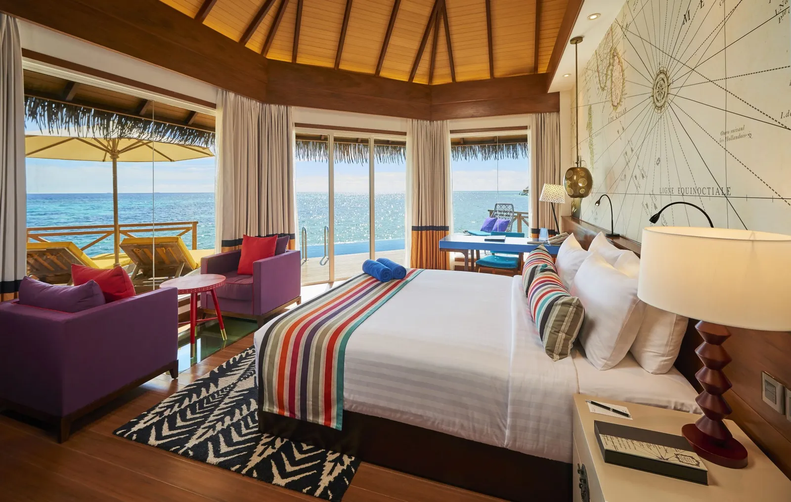 An Overwater Sunrise Pool Villa bedroom, its glass doors open onto the deck, the pool and the sea.