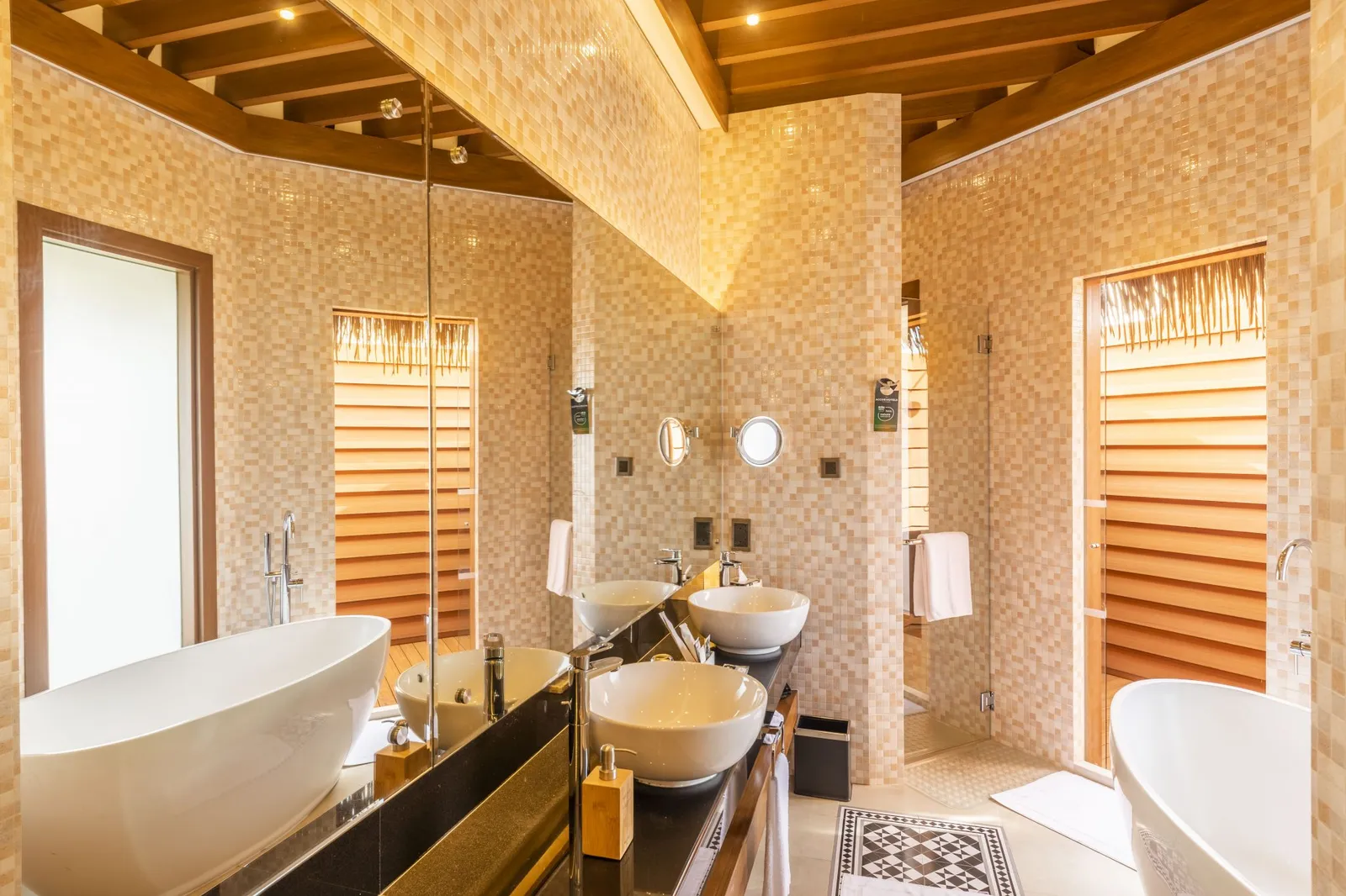 An Overwater Sunset Villa bathroom, with a freestanding tub, 2 basins and a glass shower.