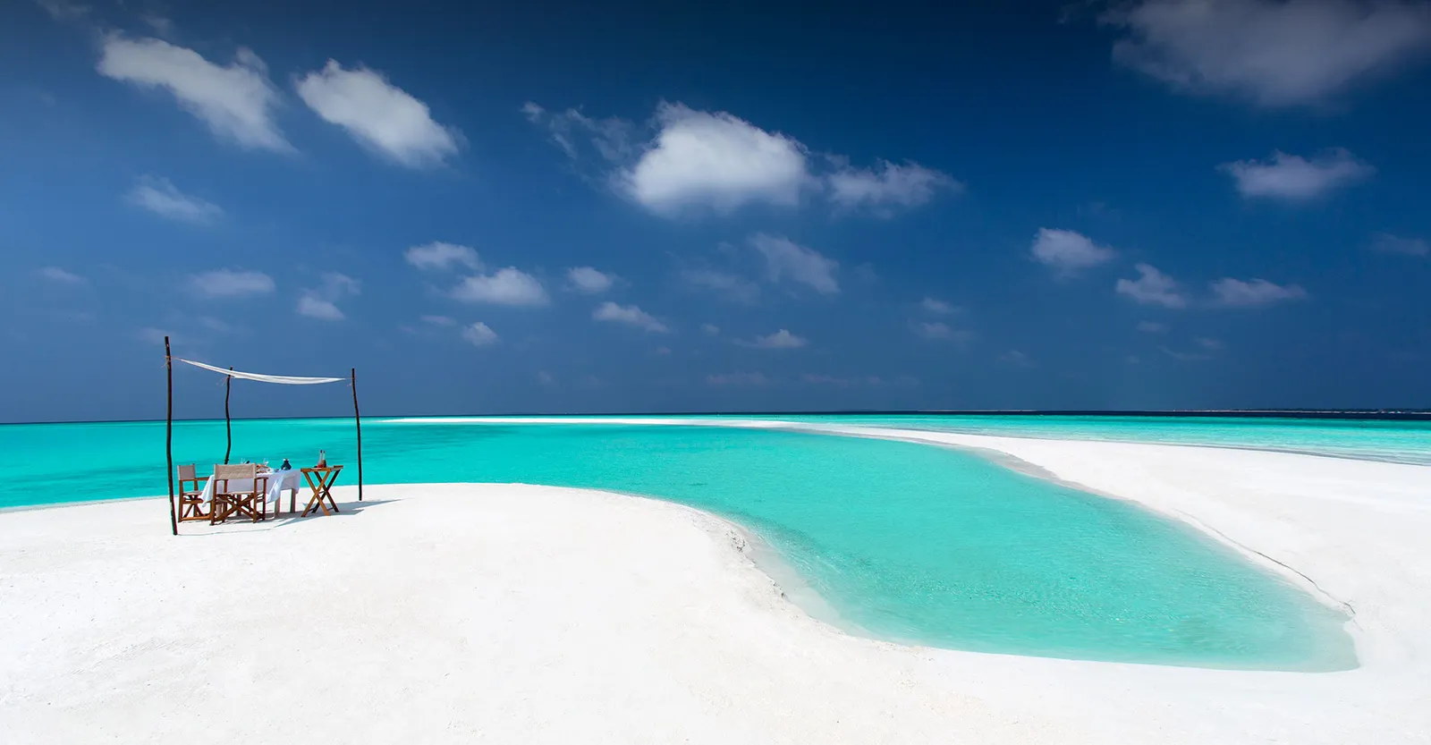 A table for 2 under a white canopy on the sandbank in the middle of the lagoon
