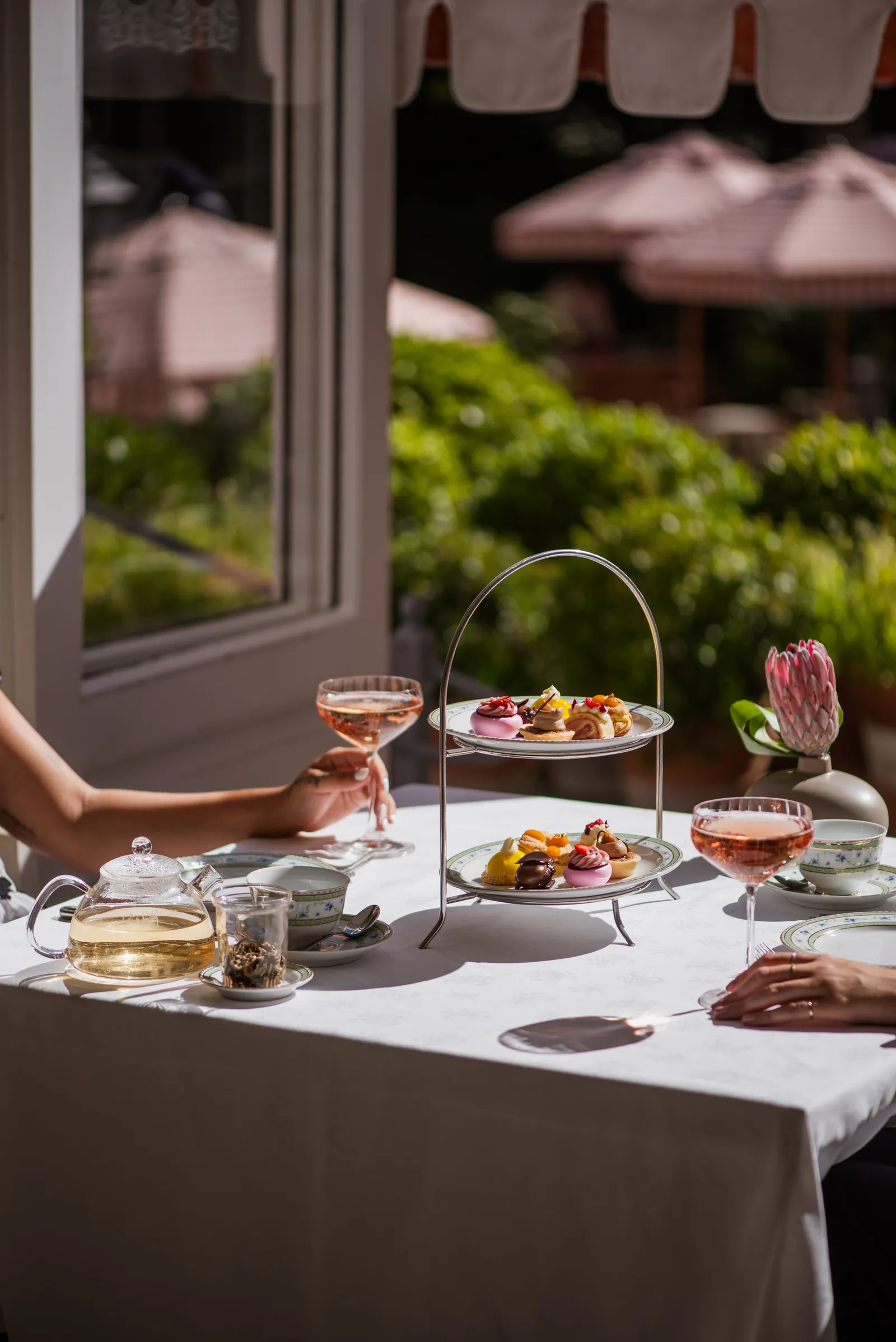 The tea table with a 2-tier stand of pastries and 2 glasses of rosé, in the sun