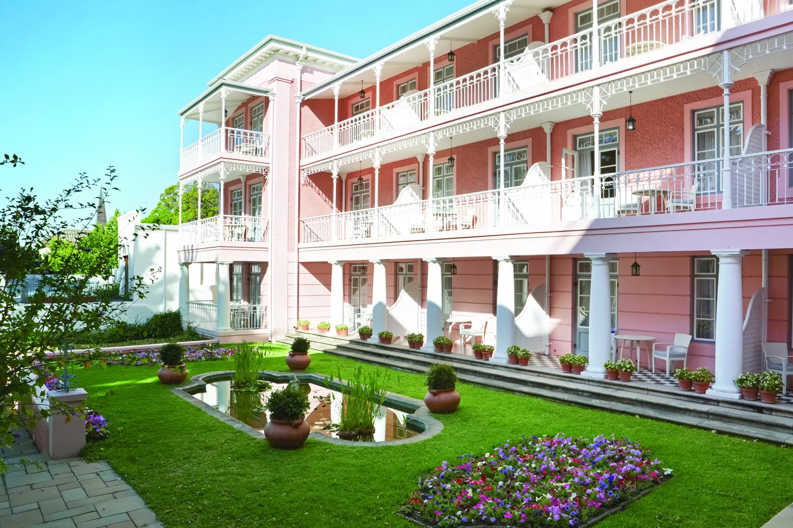 The pink façade and white verandas above the lawn and fountain