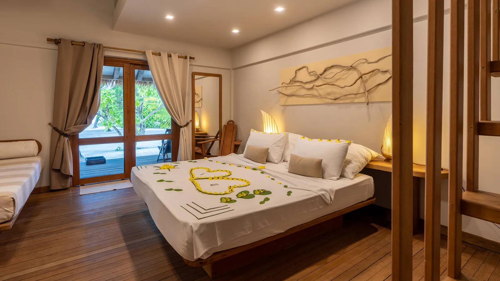 A beach bungalow bedroom: the double bed strewn with flowers and the French window open onto the green.