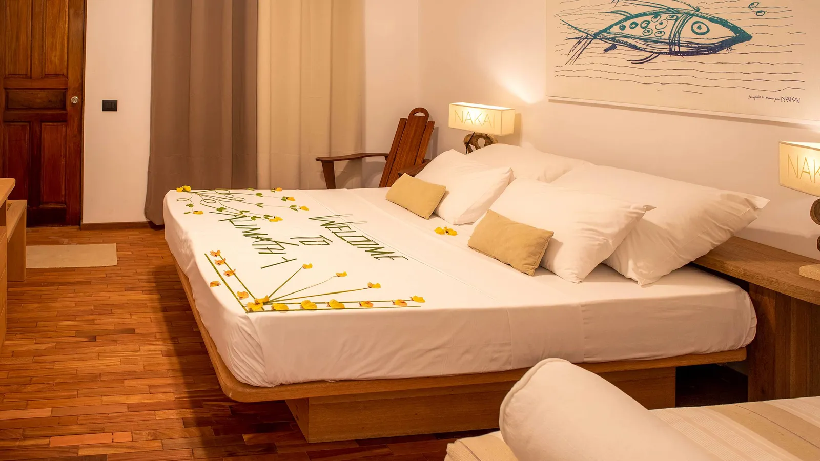 A garden room: the double bed laid with welcome flowers, the timber floor and a painted fish on the wall.