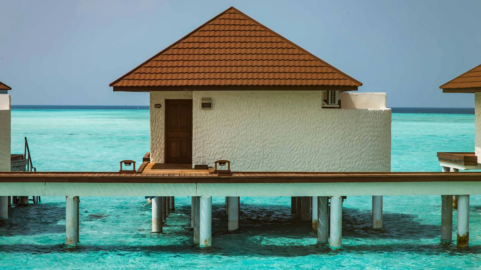 A water bungalow on its stilts, with a red-tiled roof, its deck and the turquoise lagoon all round.