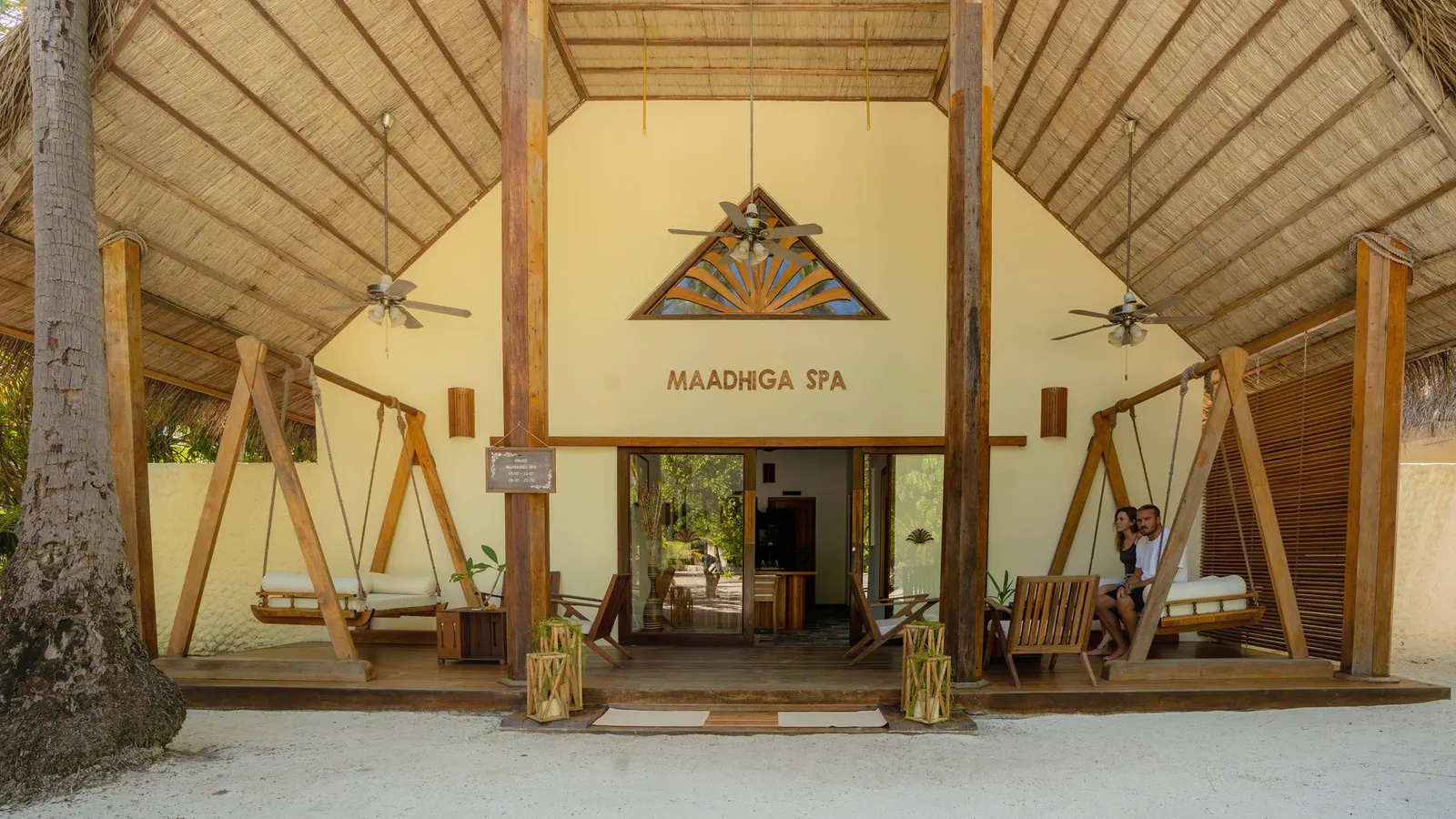The entrance to Maadhiga Spa under its thatched roof, with wooden swing seats under the porch.