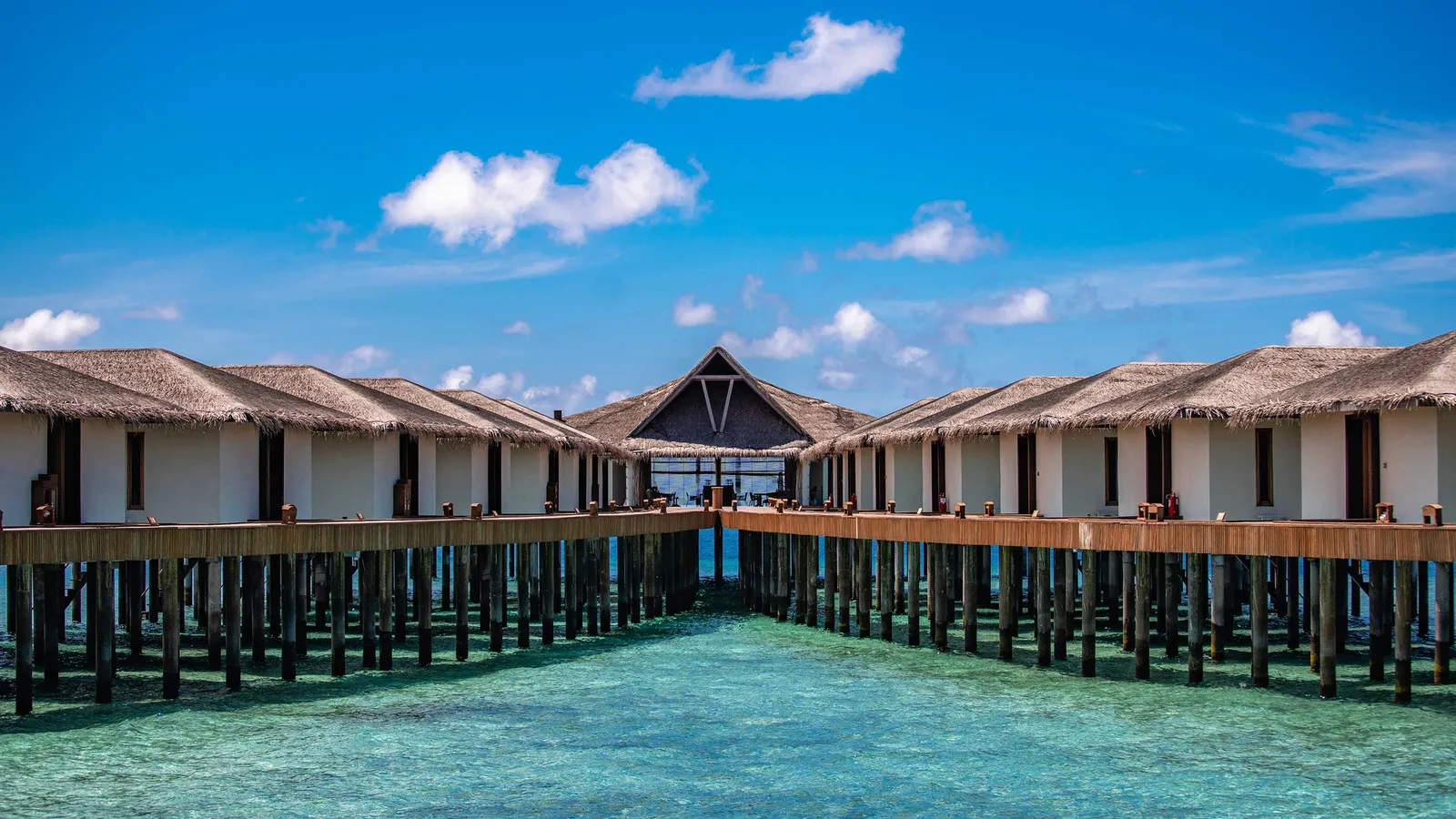 The wooden jetty leading to the water bungalows, their thatched roofs lined up above the lagoon.