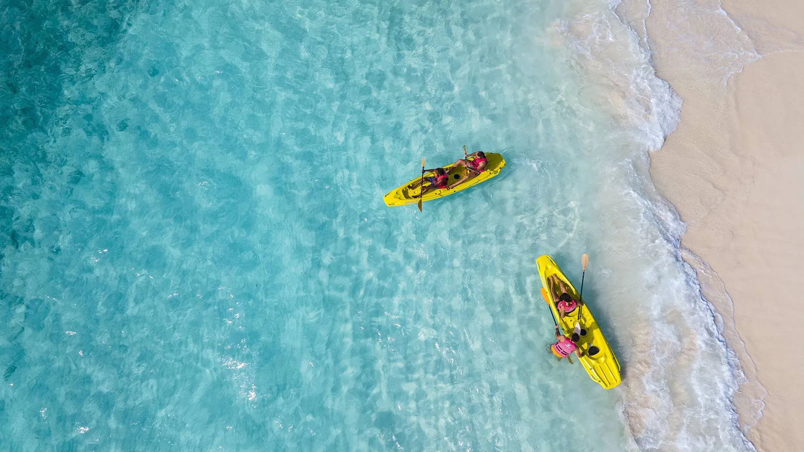 From above, 2 yellow kayaks on the turquoise lagoon beside the white shore.