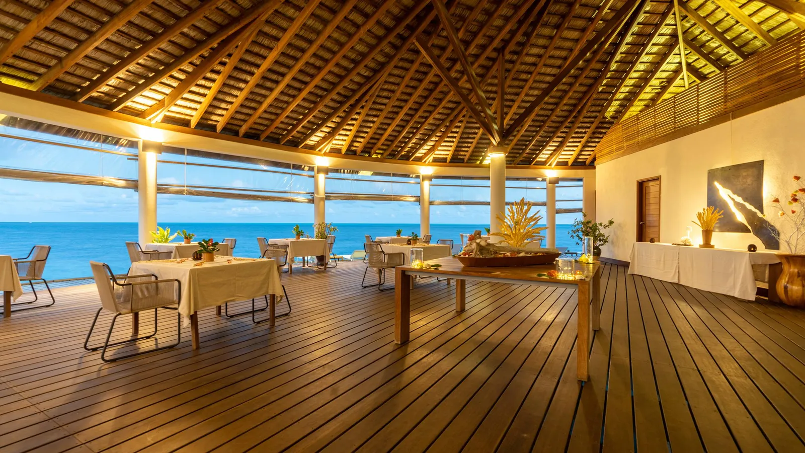 The restaurant over the water at the end of the jetty: laid tables on the boards, the thatched roof and the sea.