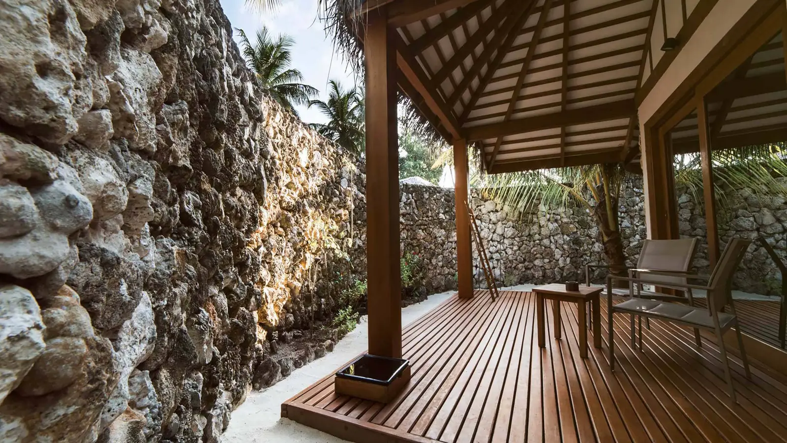 The garden villa’s veranda, closed by a coral wall, with a table and chairs.
