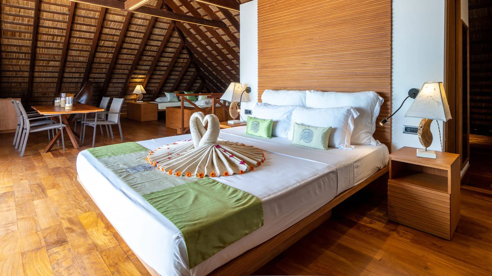 The upper-floor suite’s bedroom under the sloping timber roof, with the table and the sitting area.