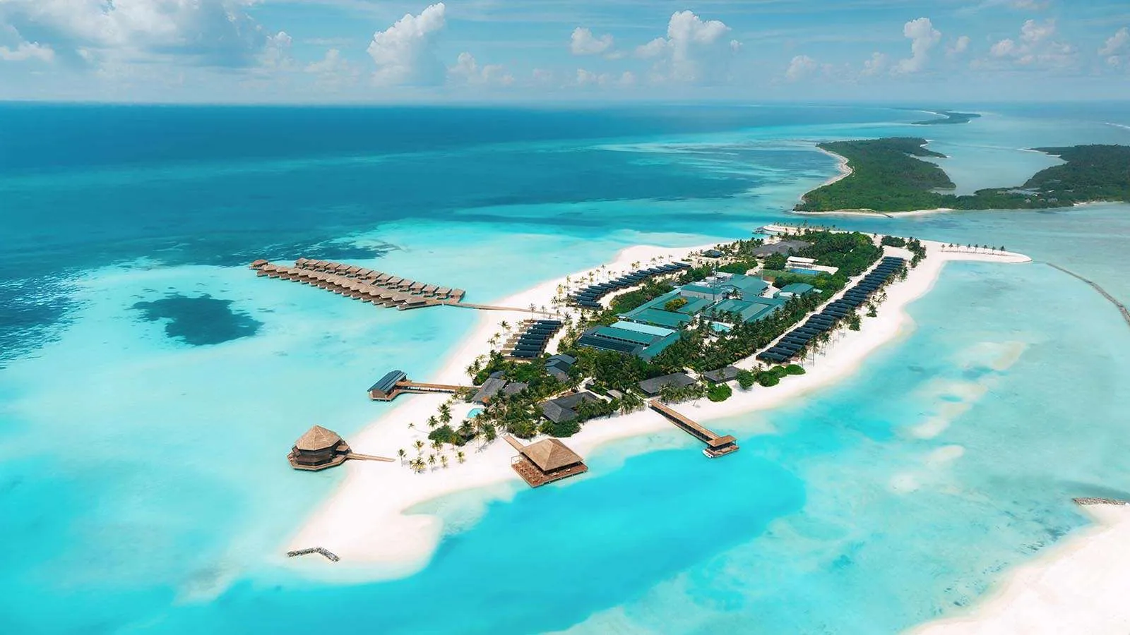 L’isola intera vista dal cielo: la macchia verde, la spiaggia bianca e le 2 file di ville sull’acqua nella laguna turchese.
