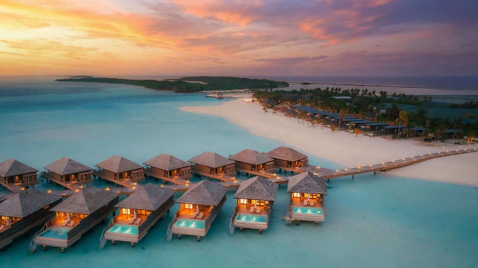 Le Ocean Pool Villa al tramonto, con le luci accese e la passerella di legno sulla laguna.