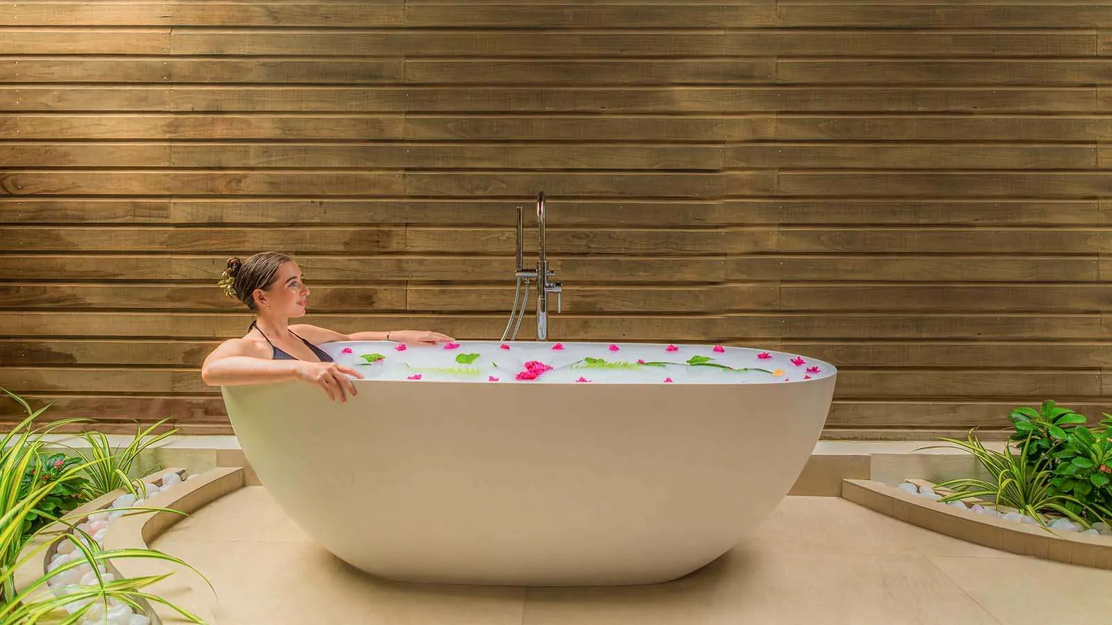 La vasca all’aperto di una Romantic Beach Villa, con i petali, davanti alla parete di legno.