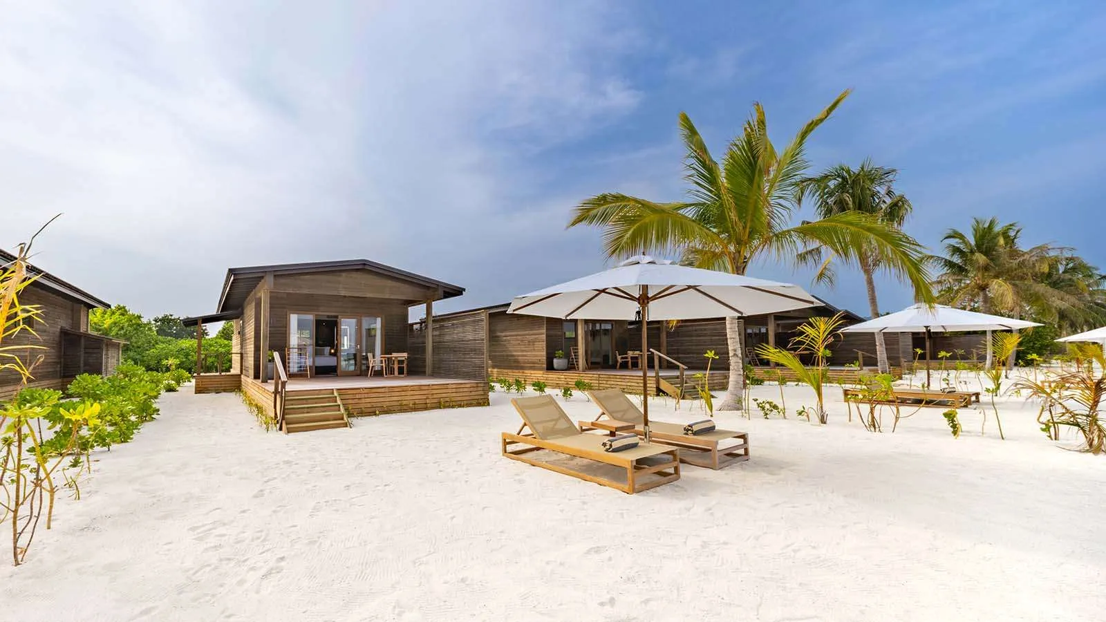 Una Sunrise Beach Villa sulla sabbia, con la veranda di legno, 2 lettini e gli ombrelloni.