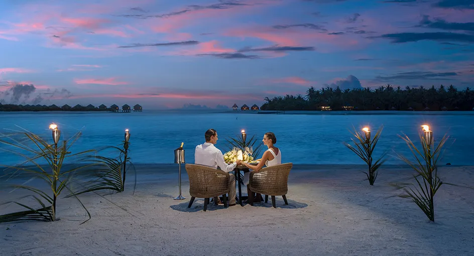 Dinner for 2 on the beach at dusk, between lit torches, with the lagoon and the islands behind.