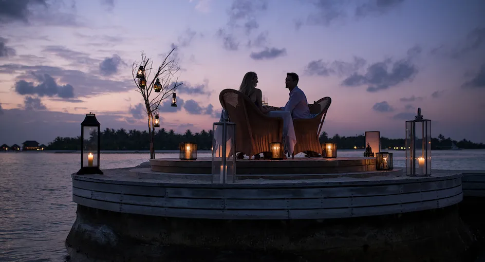 A private dinner on a round platform over the lagoon at dusk, lanterns lit and 2 guests at the table.