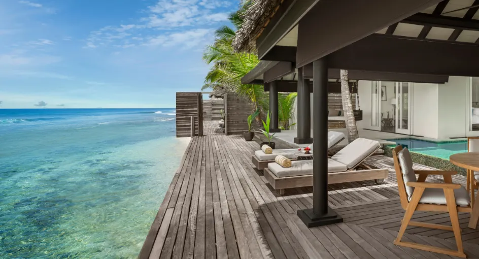 The Two Bedroom Ocean House deck: timber boards, loungers and the pale lagoon beyond the rail.