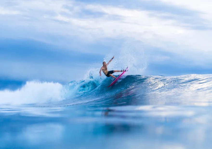 A surfer on the face of a blue wave, amid the spray.