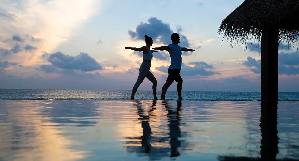 2 people doing yoga at sunset on the edge of an infinity pool that mirrors the sky.