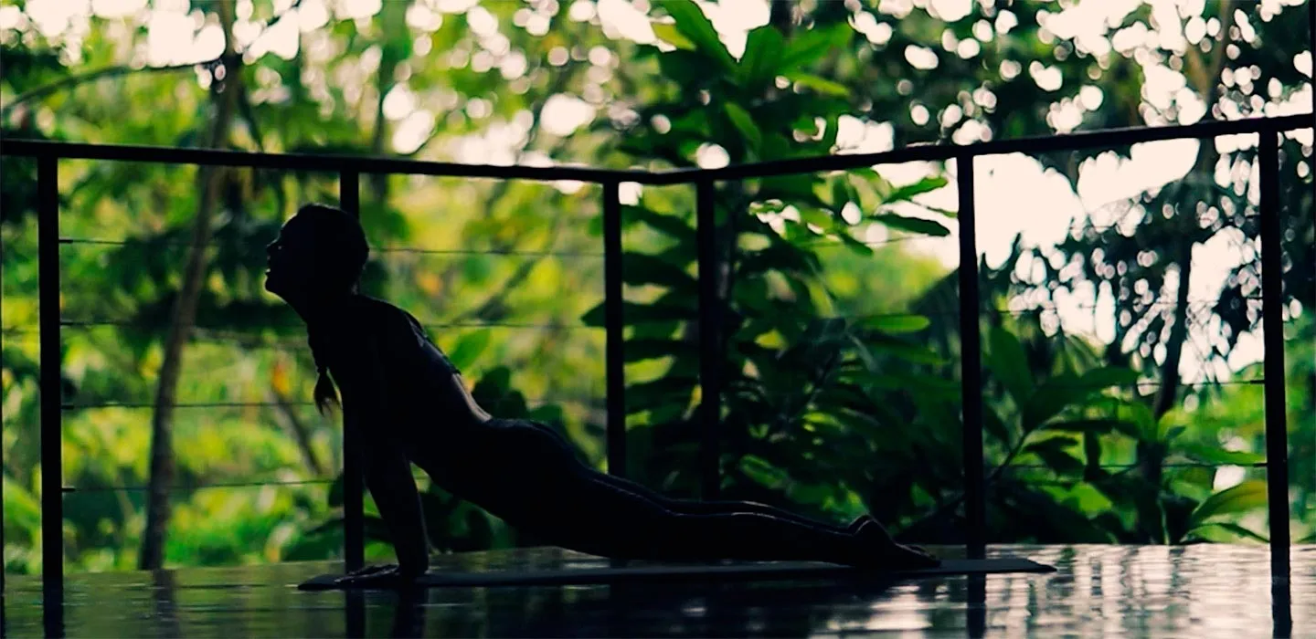 A person practising yoga on a mat in the pavilion open to the rainforest