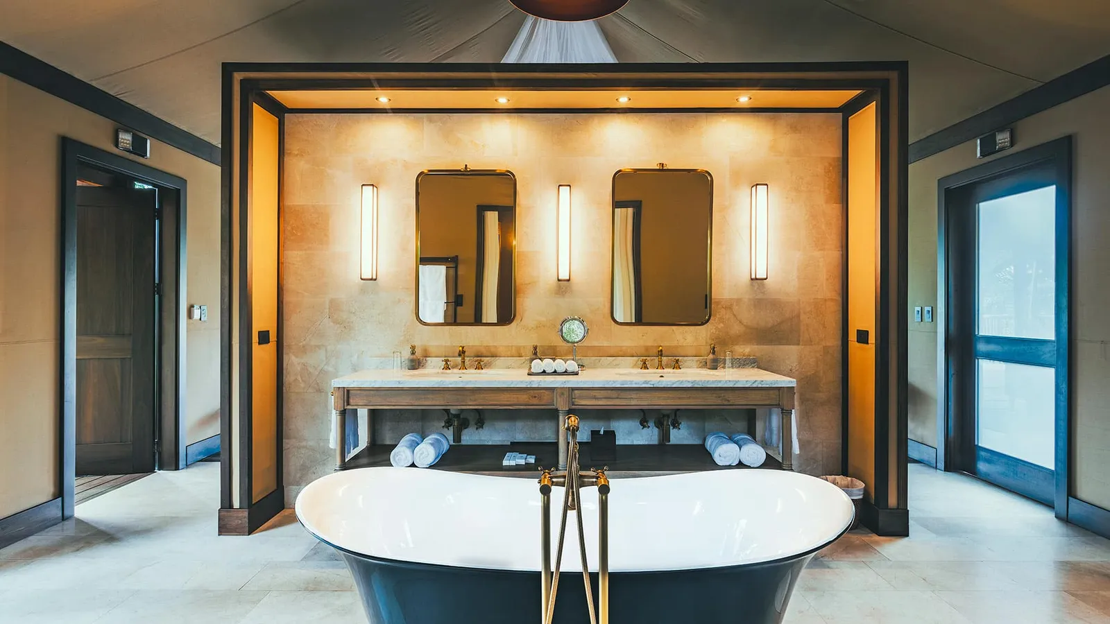 A freestanding bath in front of 2 basins and mirrors