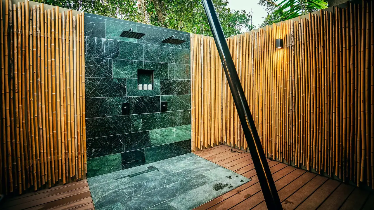 An outdoor shower in green stone, enclosed by bamboo screening