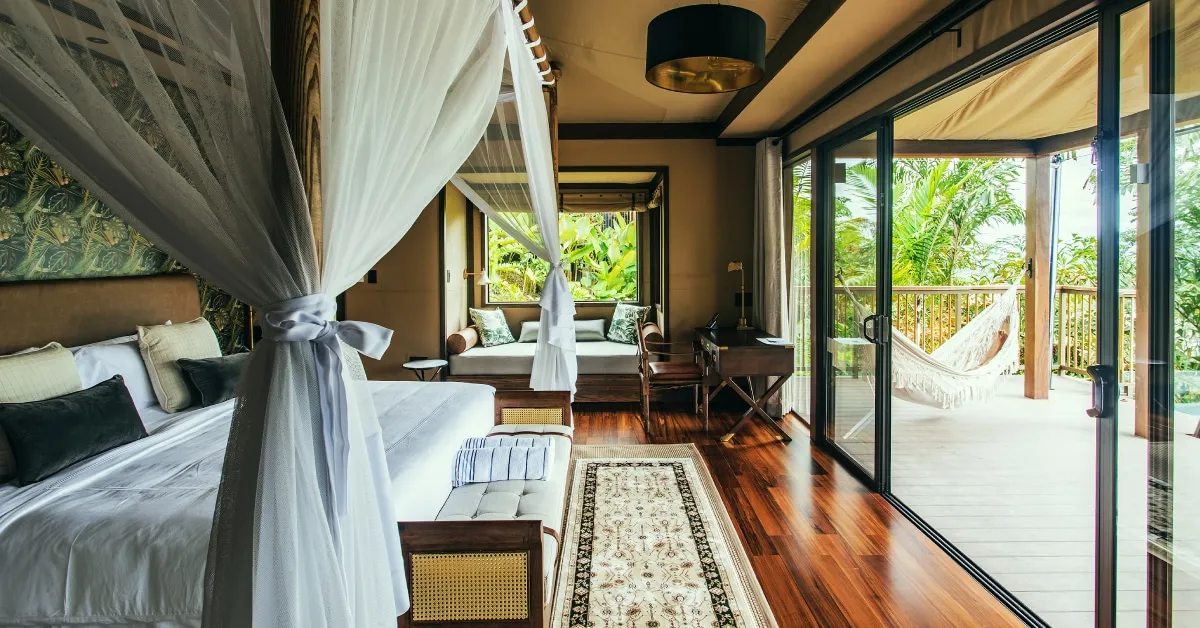 The Nayara Tent’s four-poster bed, with a terrace and hammock beyond the glass doors