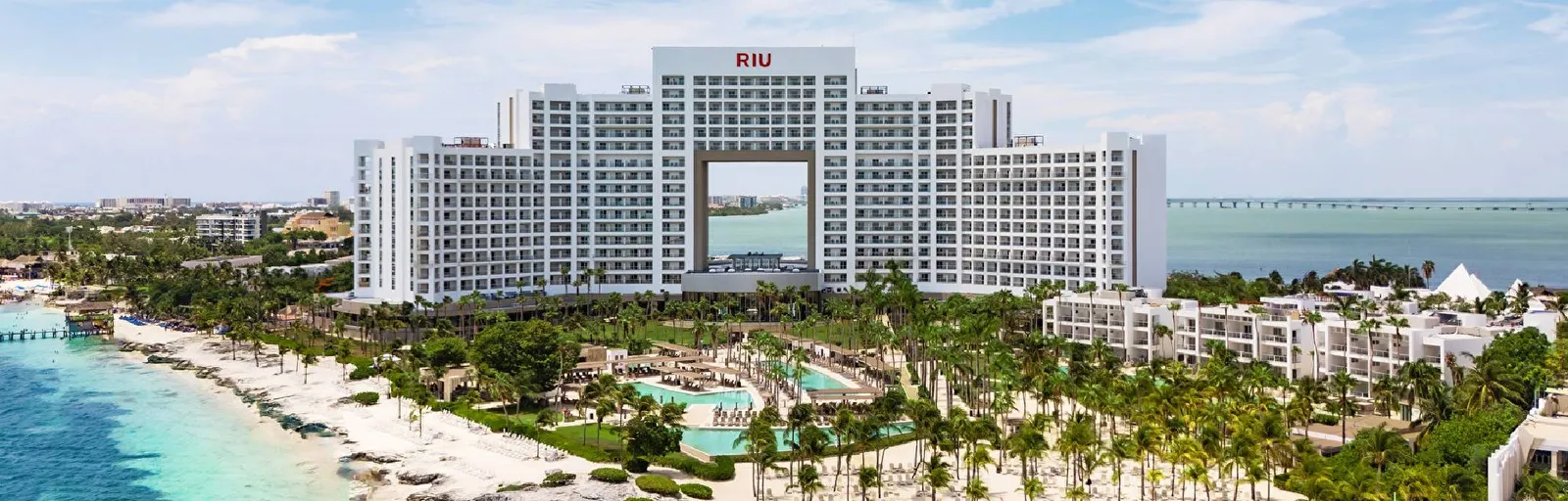 The Riu Palace Peninsula’s white tower with its central arch, the pools among the palms and the beach on turquoise water