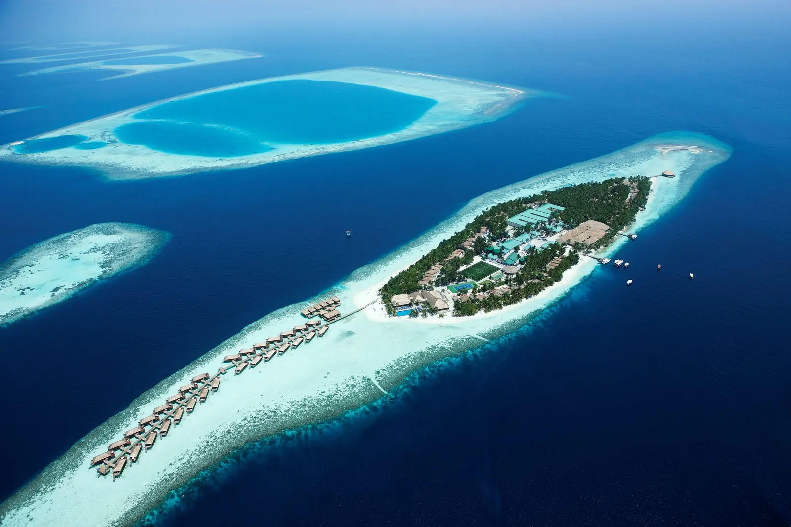 Vilamendhoo from above: the green island in its reef, the white beach and the water-villa jetty