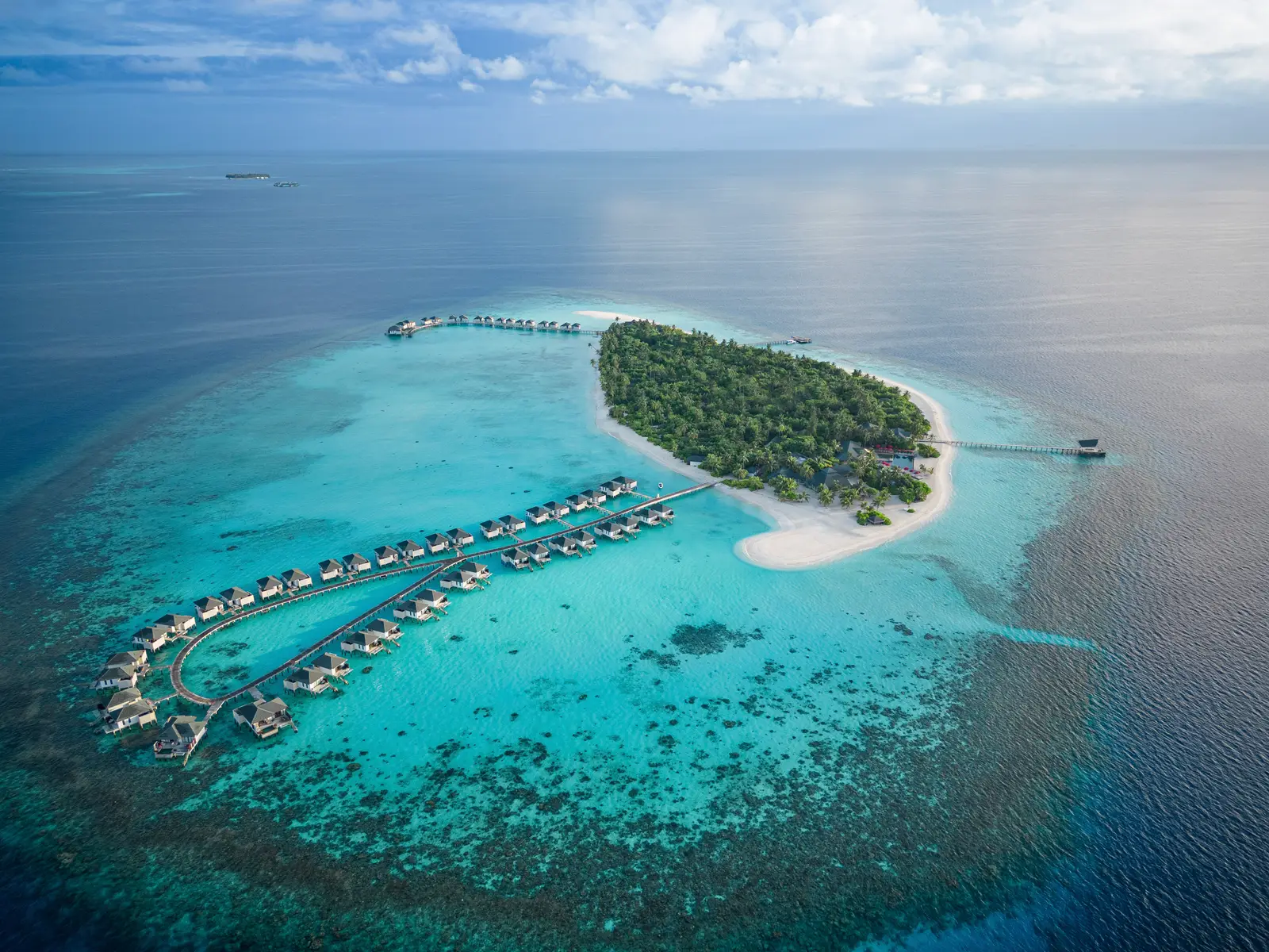 The island from above: dense green, the white beach and the 2 jetties of water villas reaching out over the reef.