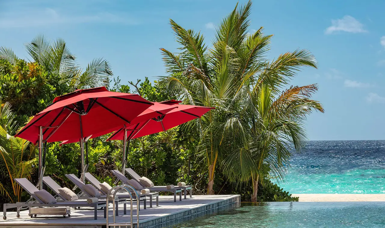 The main infinity pool at the tip of the island, its loungers under red parasols and the sea behind.