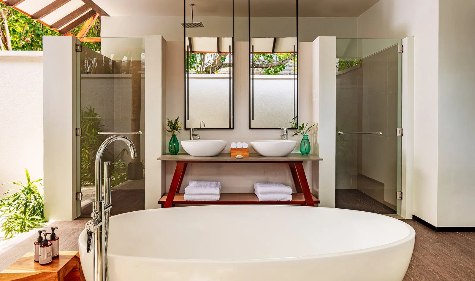 A water villa bathroom: the freestanding tub, the 2 basins and the shower, lit from the garden.