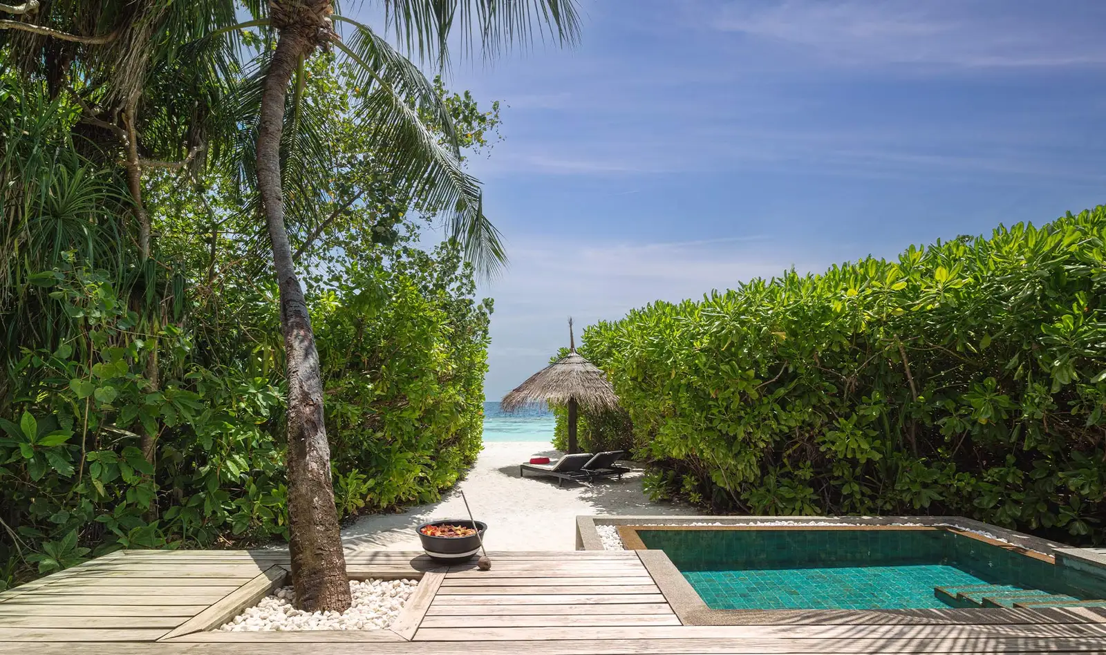 The deck of a sunrise-side pool villa among the green, with the path running down to the beach.
