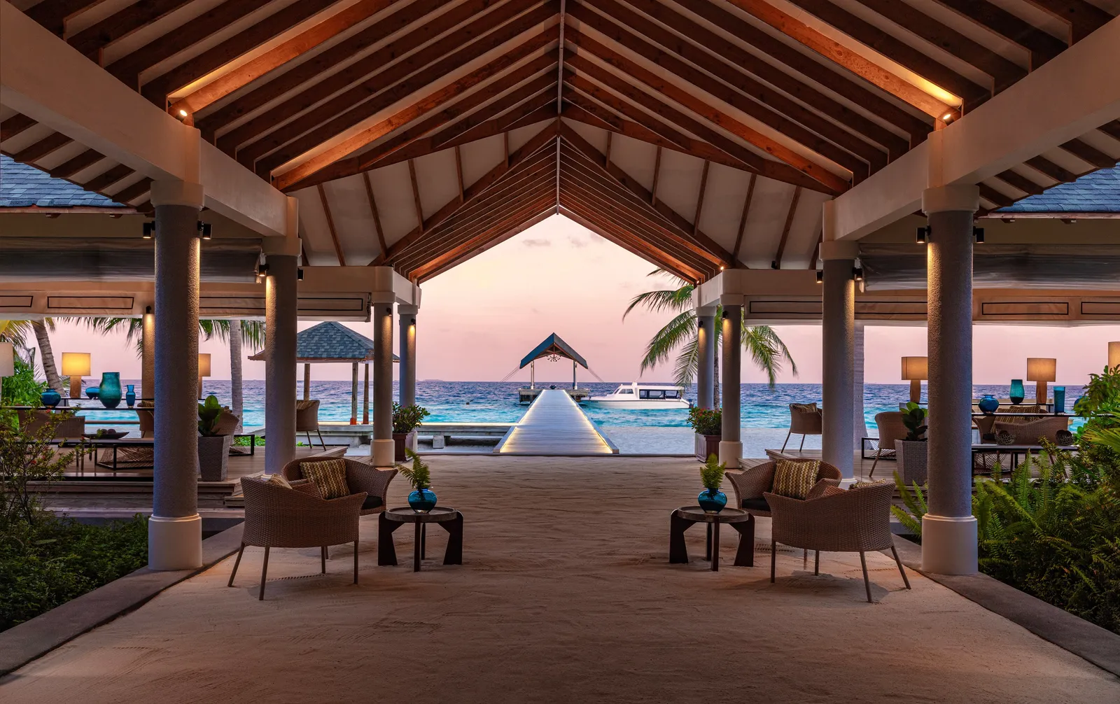 The lobby at dusk under its pitched timber roof, framing the arrival jetty and the sea.