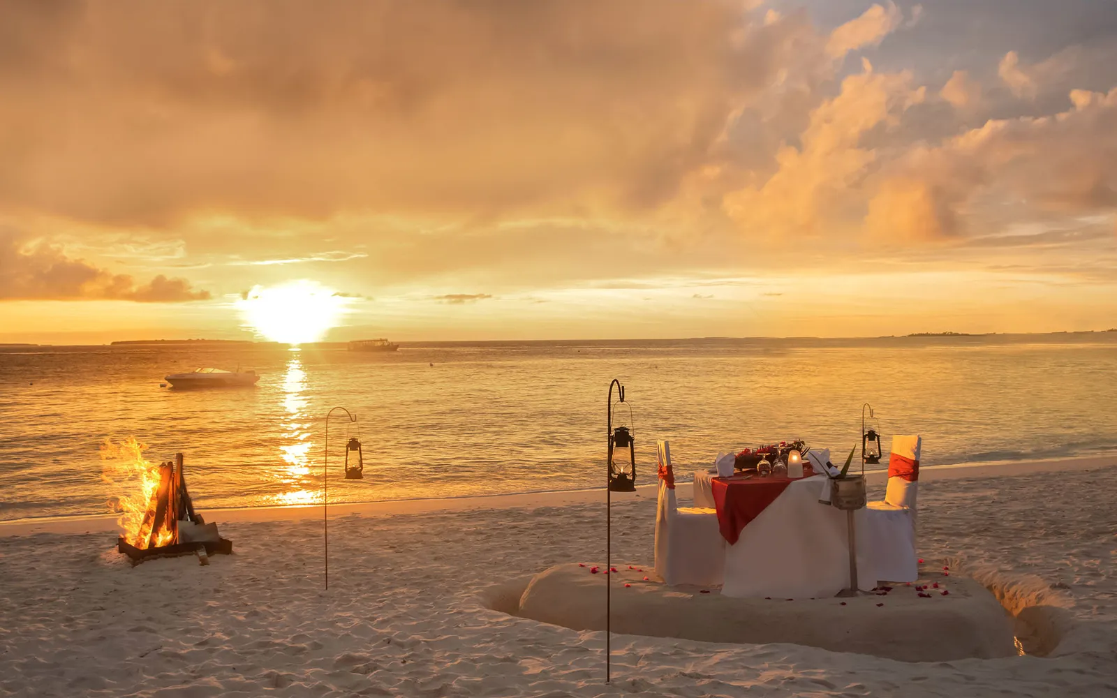 Dinner for 2 on the beach at sunset, the table laid, lanterns on poles and a bonfire on the sand.