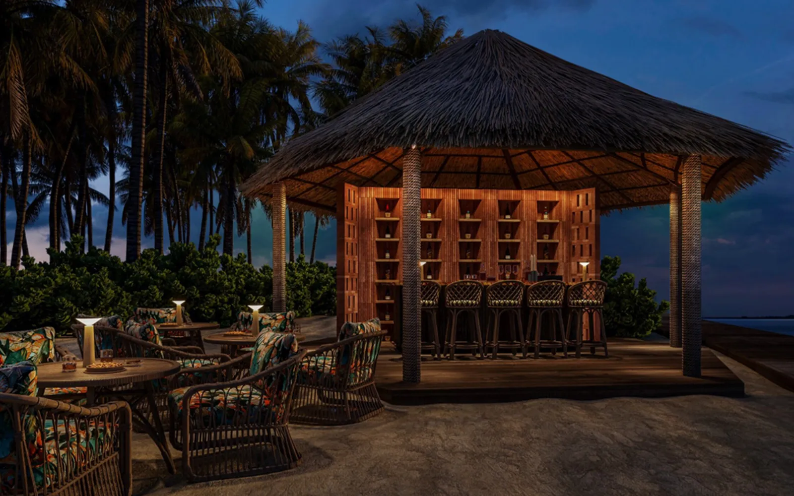 Handhuvaru at night: the lit thatched pavilion, the bottles on its timber shelves and the armchairs on the sand, among the palms.
