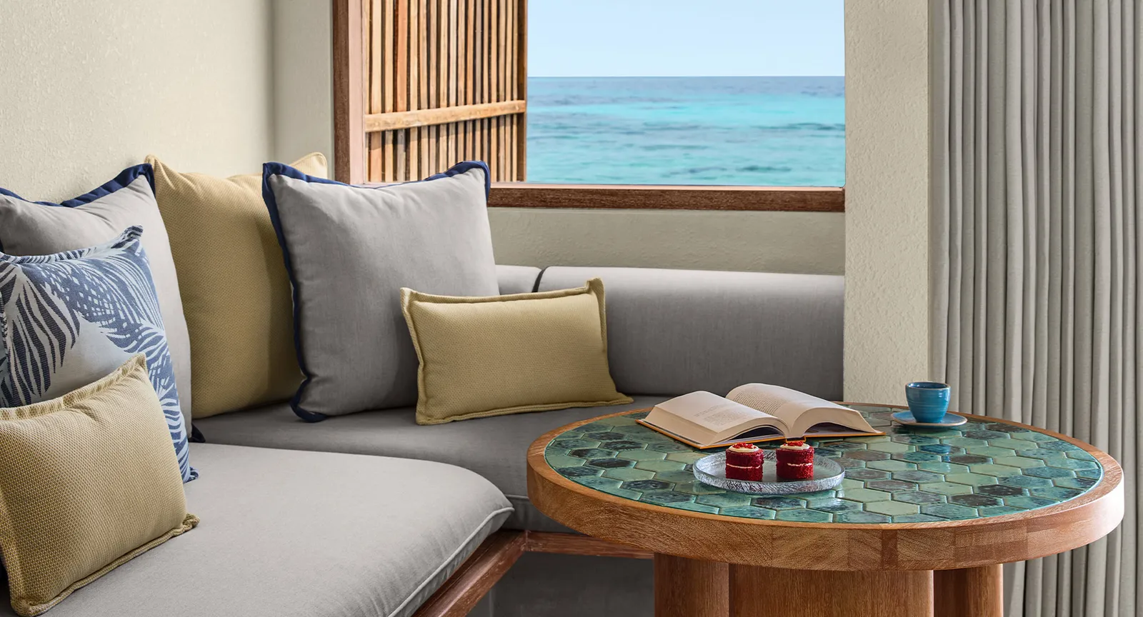 The lounge corner of a water villa, with its cushions, the tiled table and the window onto the sea.