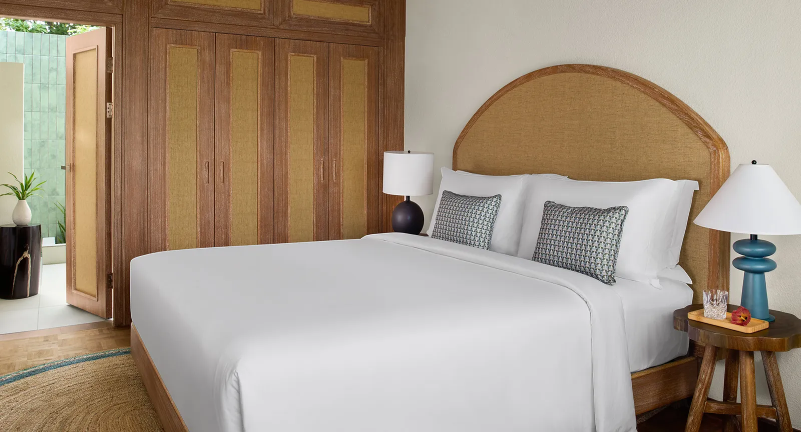 A Deluxe Sunset Villa bedroom: the white bed, the arched rattan headboard and the door open onto the green bathroom.