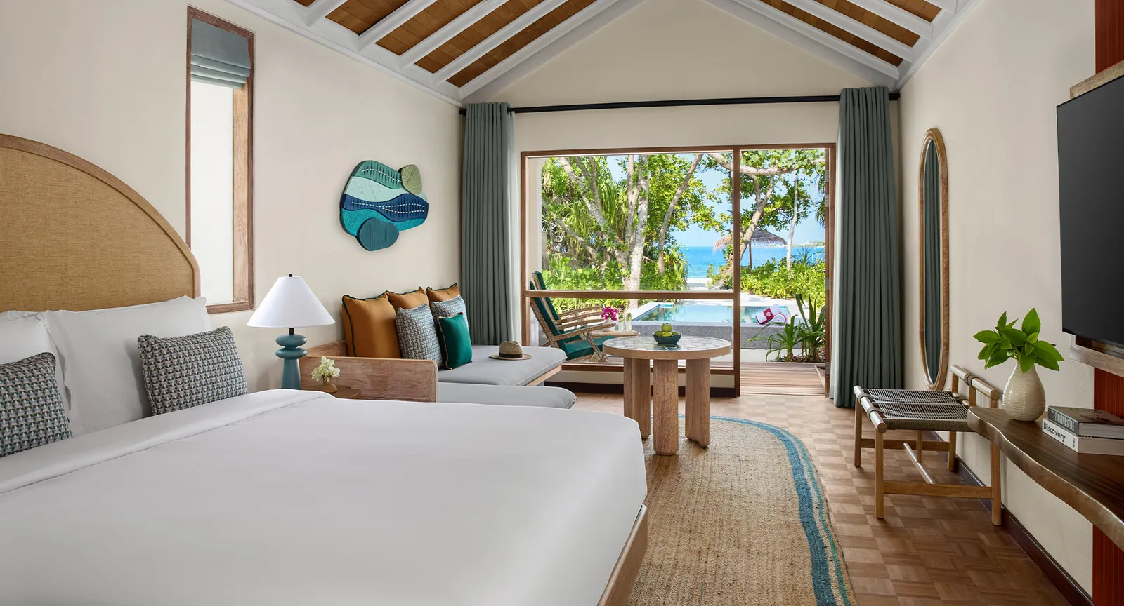 A beach pool villa bedroom, the sofa under the glass doors and the pool and the sea beyond the deck.